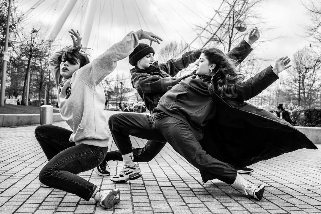 Three dancers captured mid-leap in a black-and-white outdoor photograph.