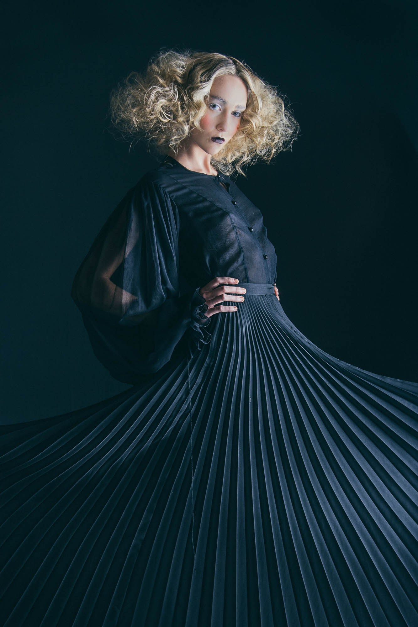 A model looking over their shoulder while holding out a dark pleated skirt.