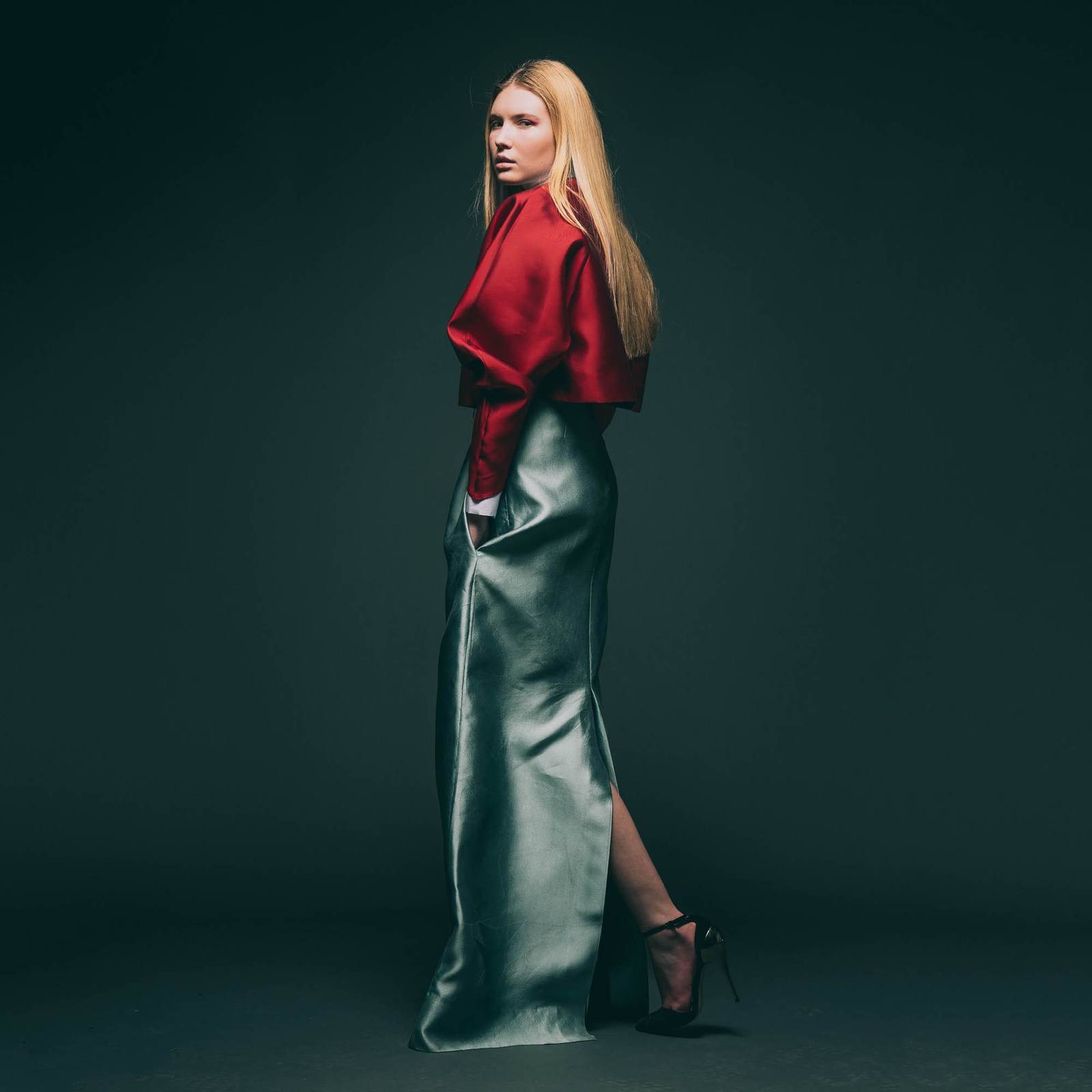Side-on studio portrait of a model in a red top and long metallic green skirt.