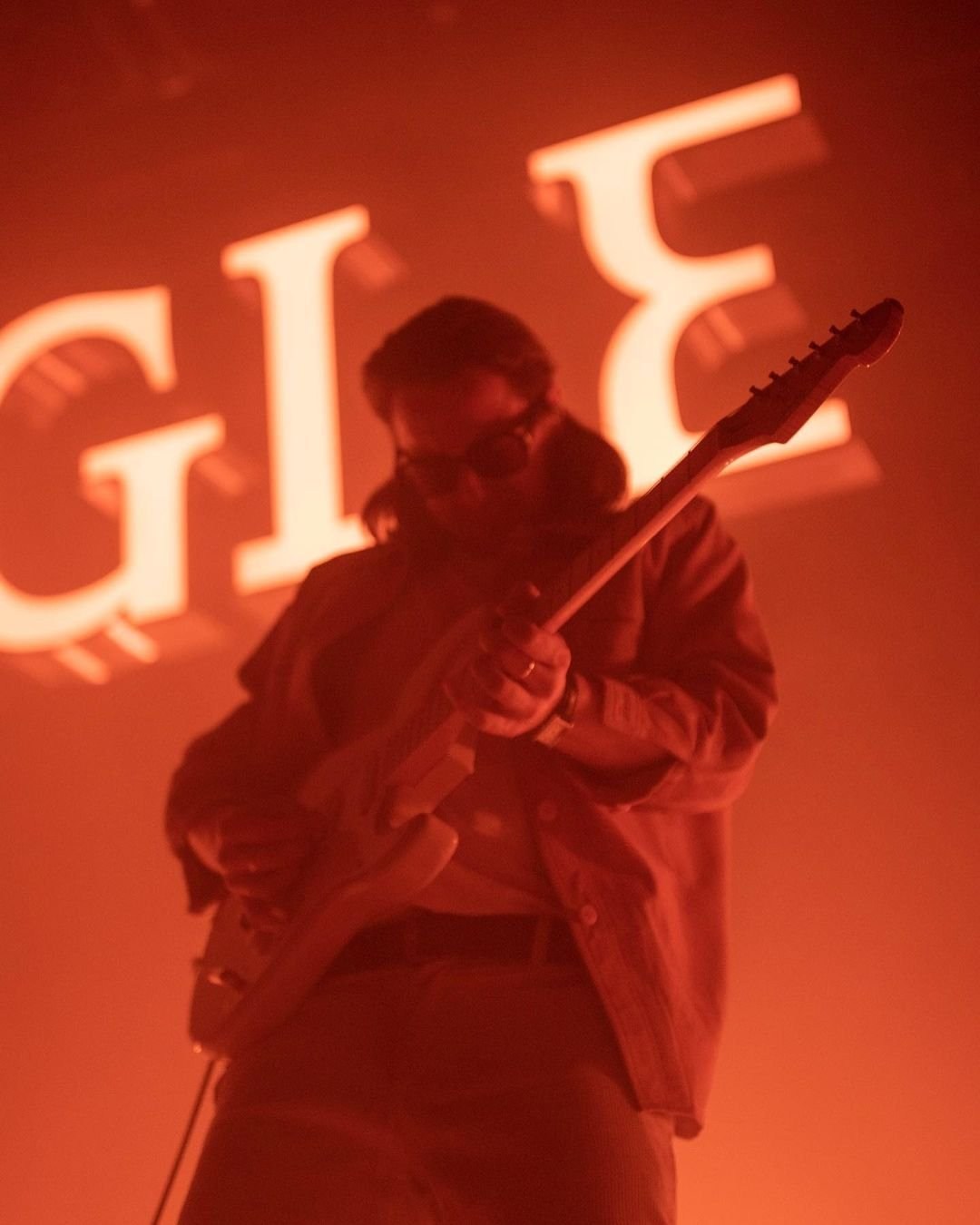 A close stage portrait of a performer raising one arm in red light.