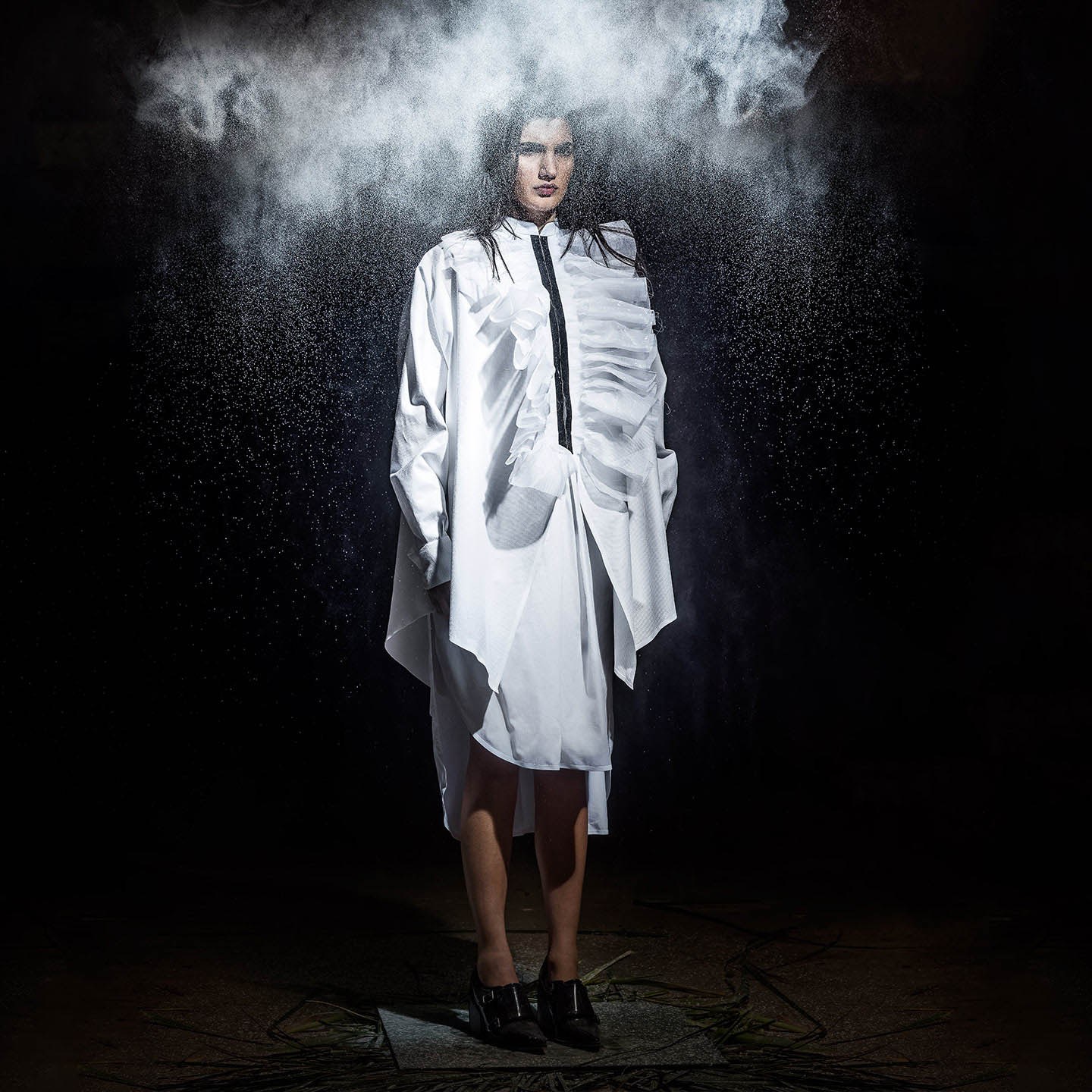 A model in a pale coat and layered white outfit beneath a cloud of smoke.