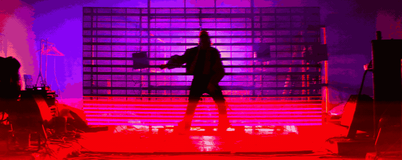 A performer on a gridded set flooded with intense red and purple light.