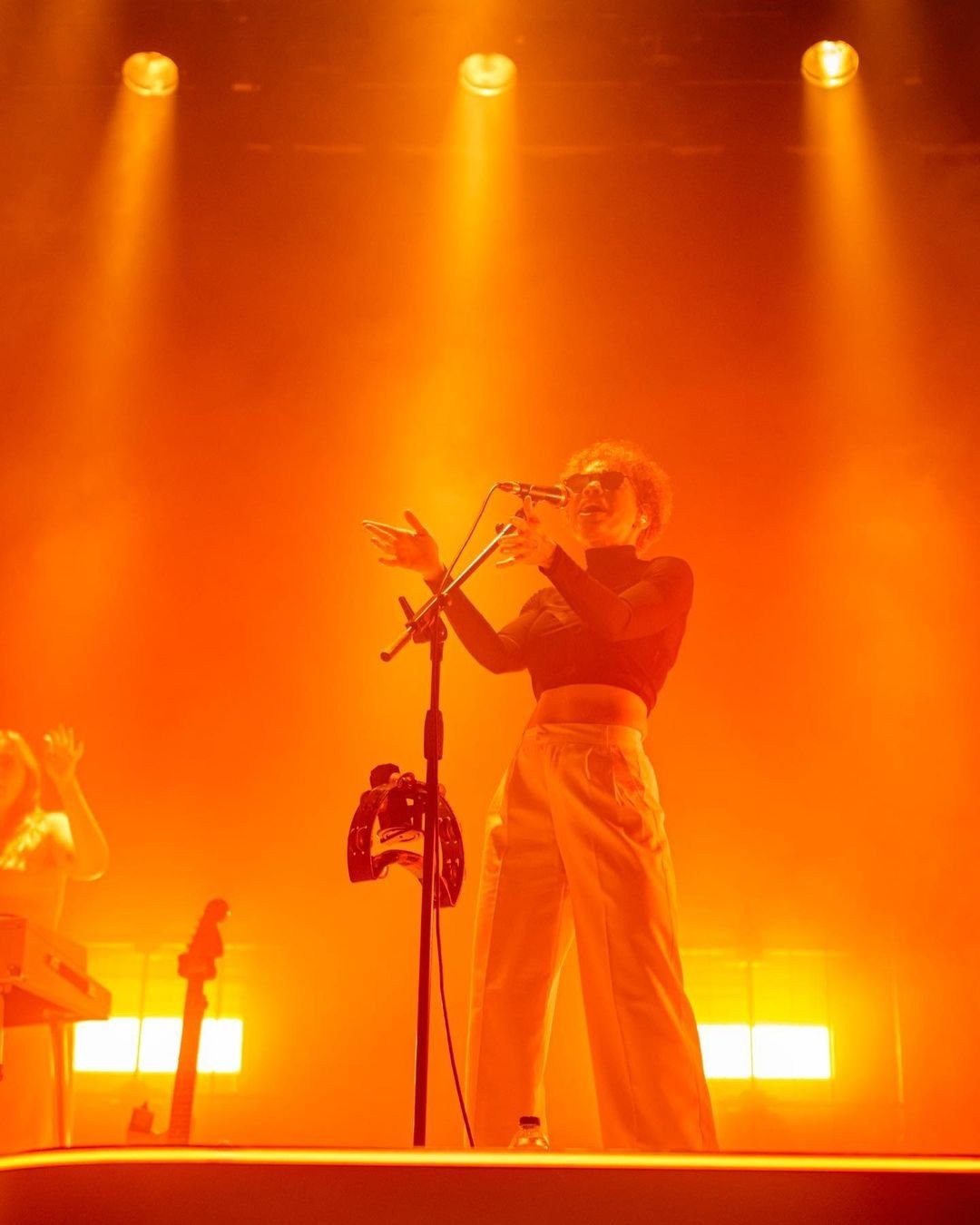 A performer leaning into a microphone amid glowing orange vertical lights.