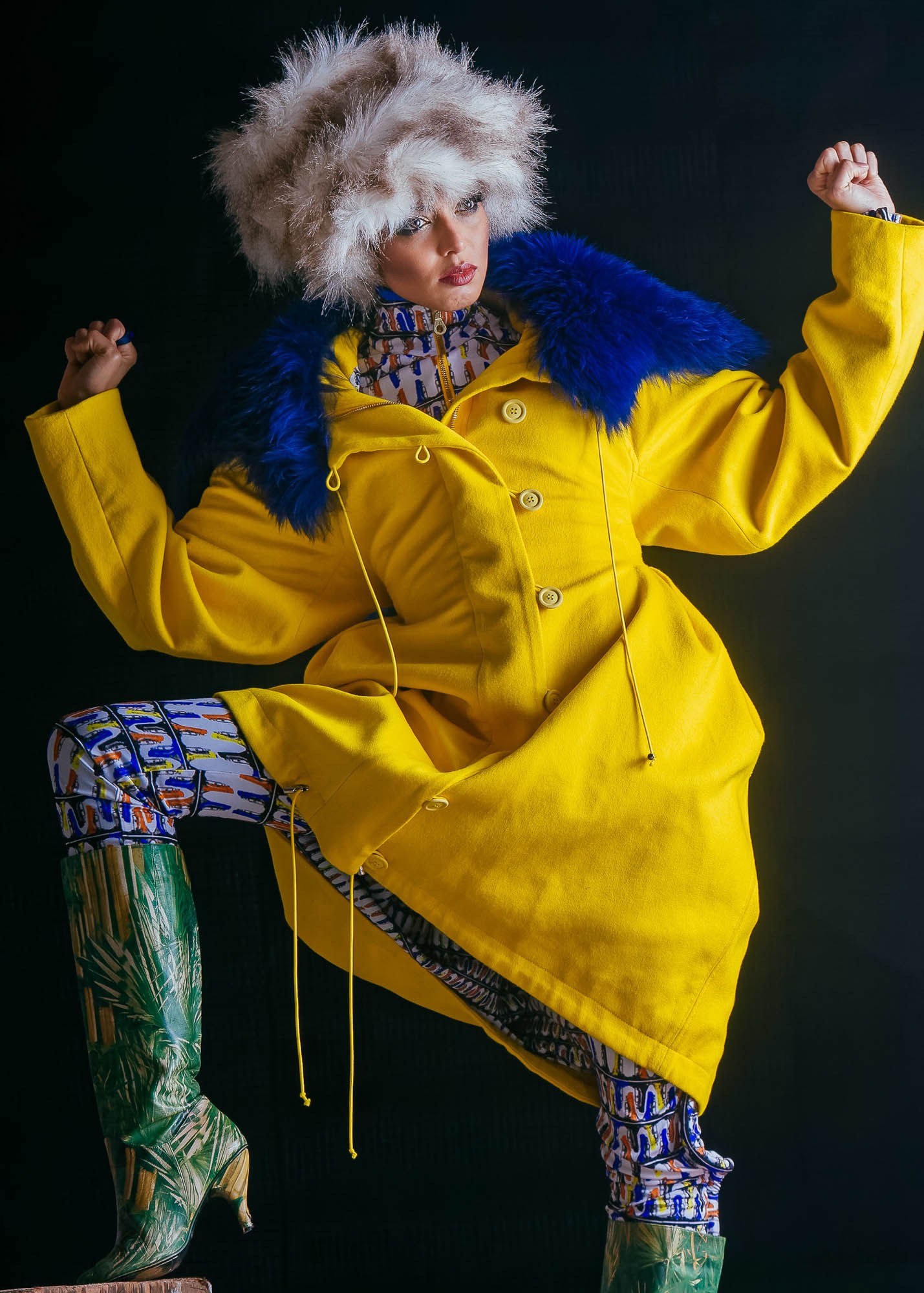 A model posing in a bright yellow coat, blue collar and patterned trousers.