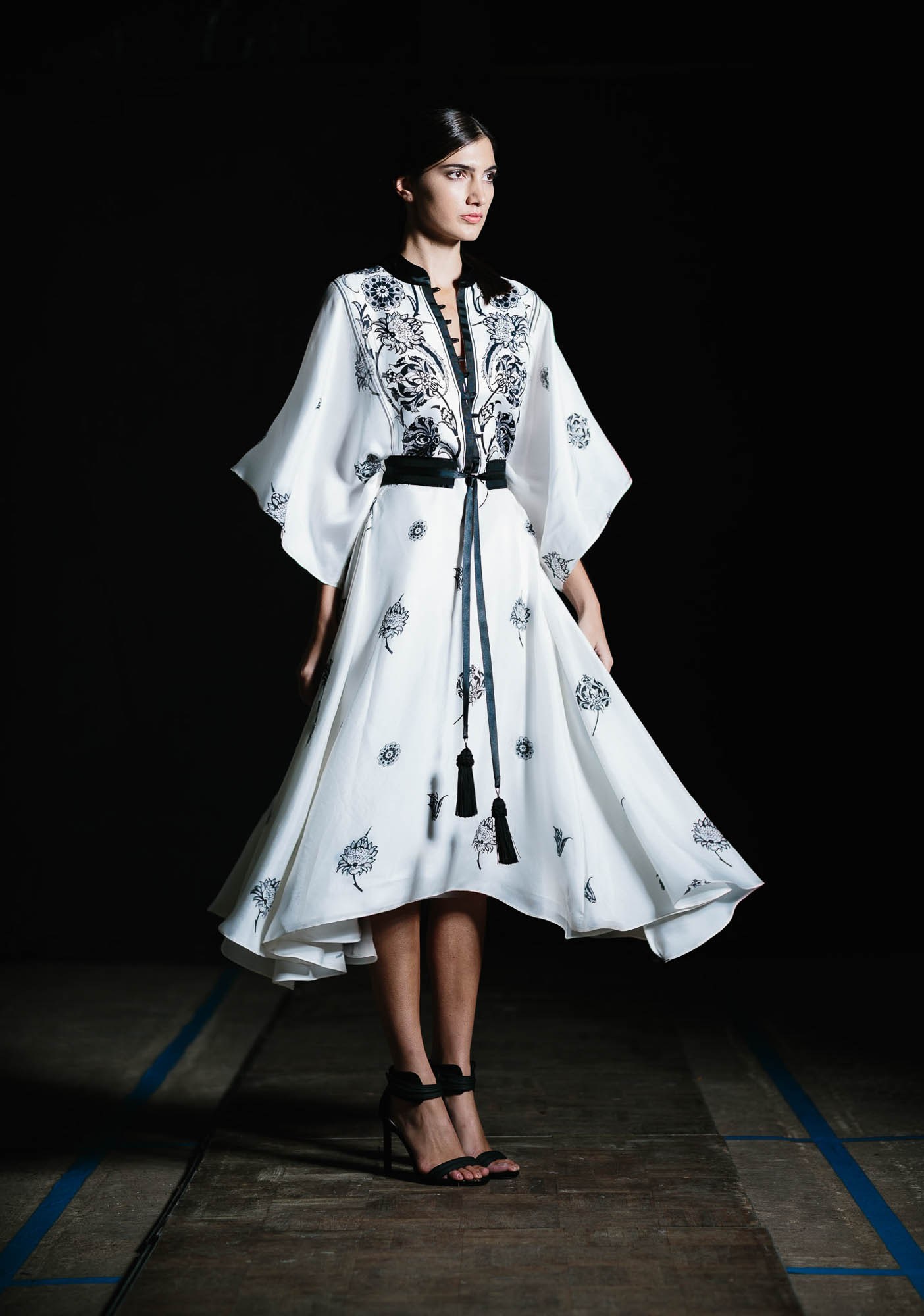 A model in a flared white printed dress photographed on a dark runway.