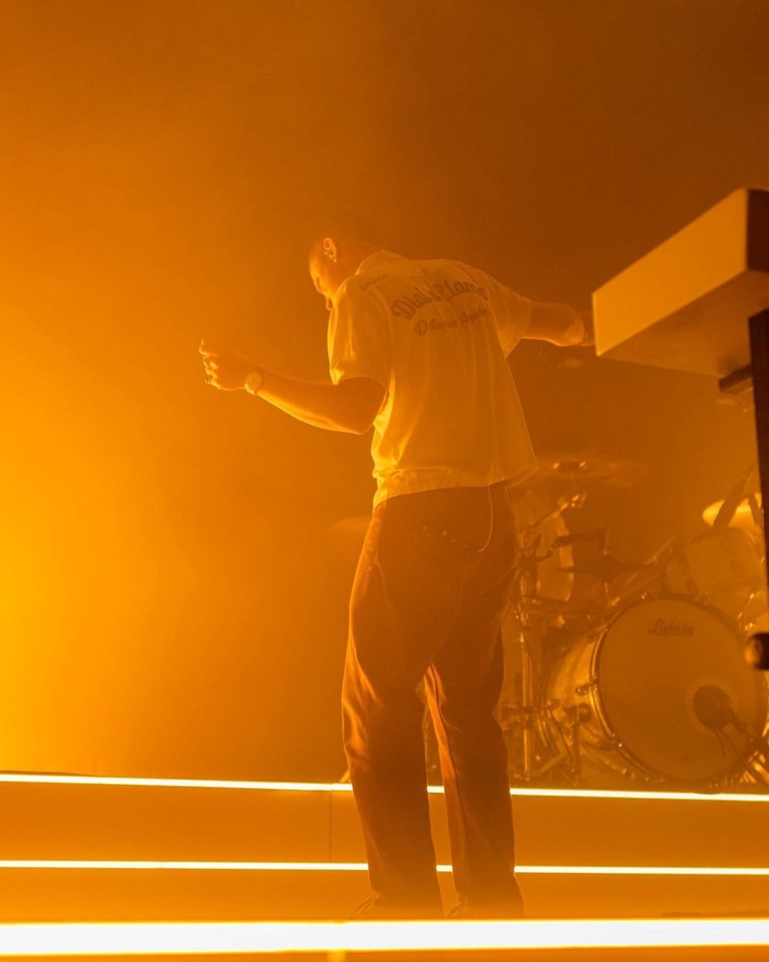 A performer lifting one arm before tall, warm-coloured stage lights.