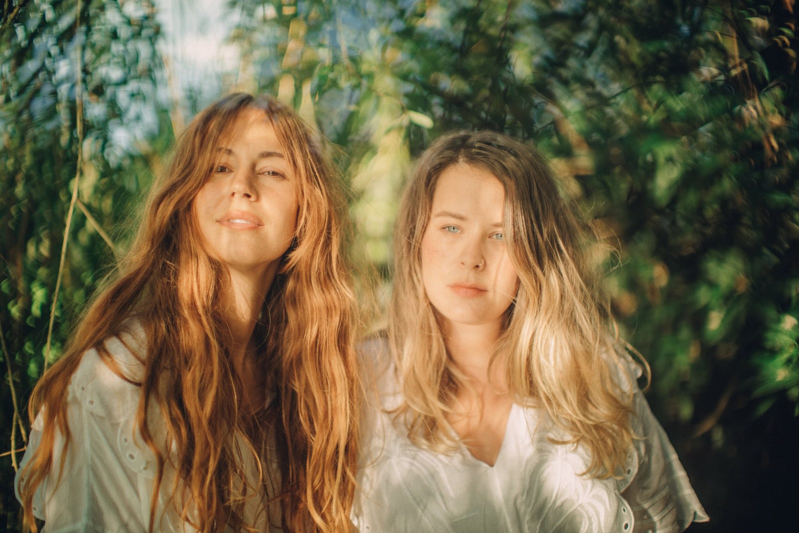 Two long-haired women in a sunlit woodland portrait.