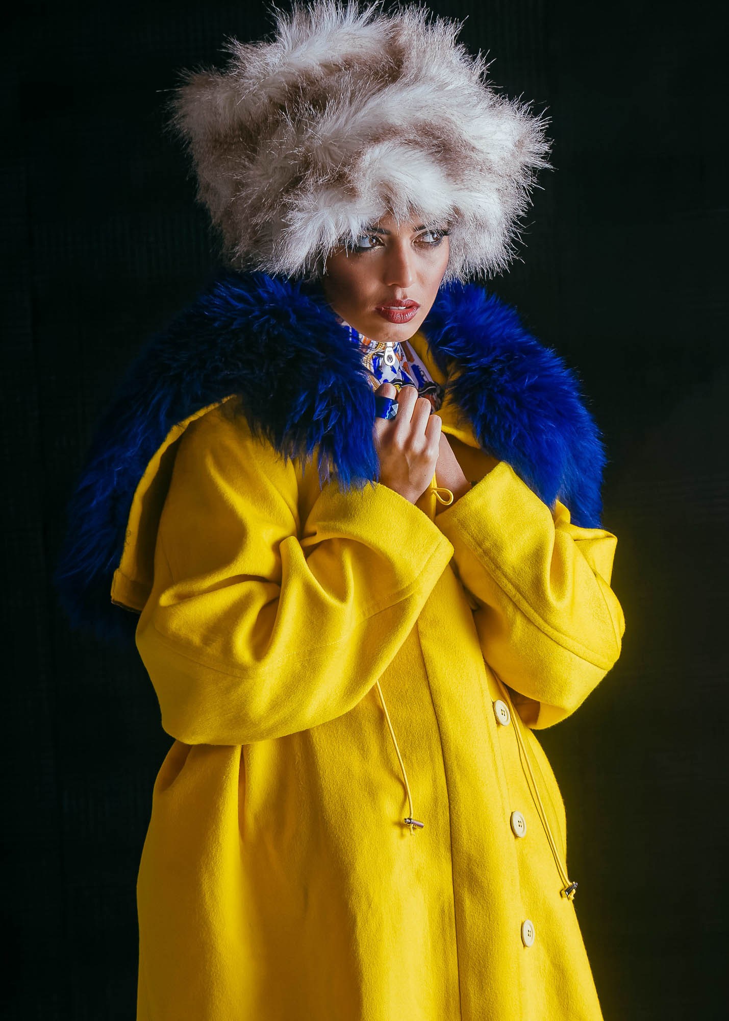 A model with a high pale hairstyle wearing a bright yellow coat with a blue collar.