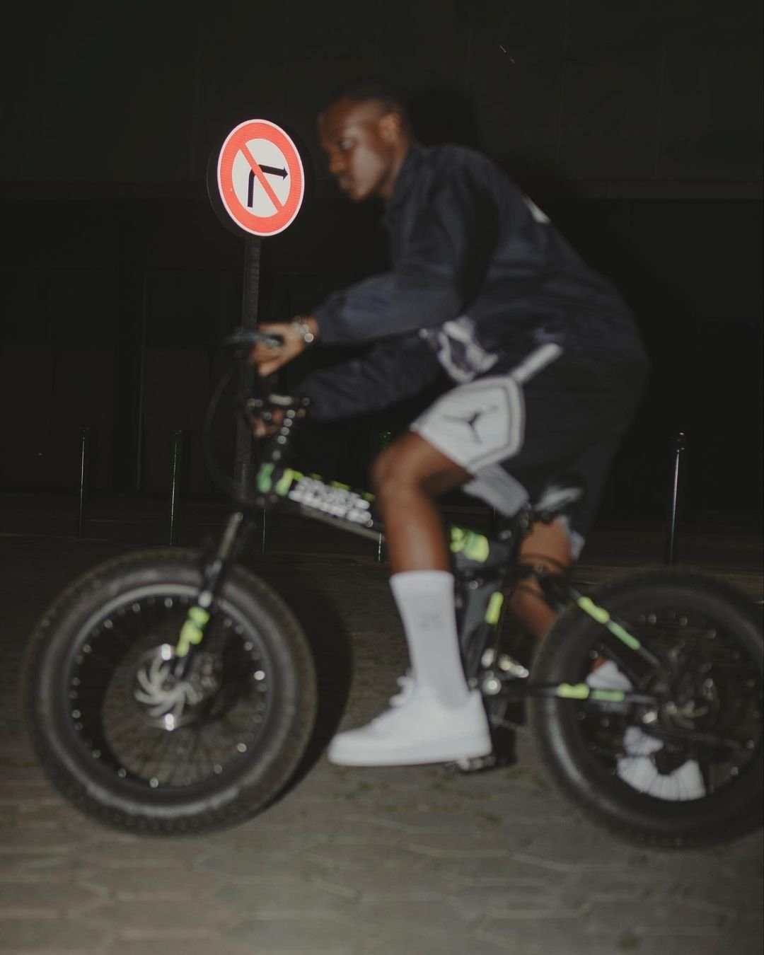 A cyclist riding along a dark street beside a circular road sign.