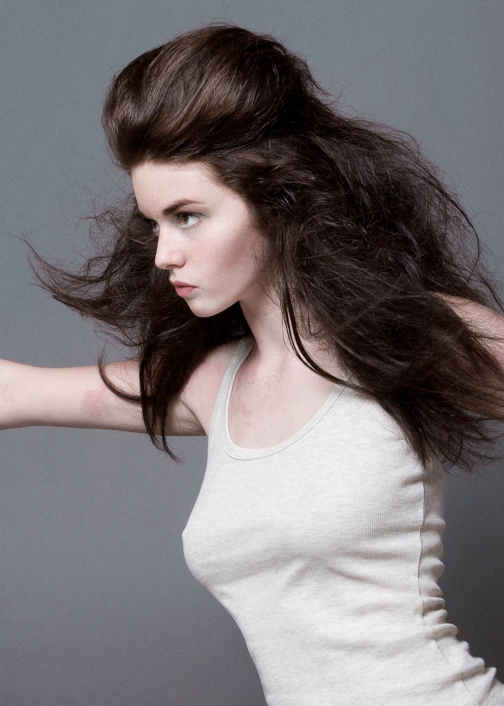 A dark-haired model in a white sleeveless top, with hair sweeping across the portrait.