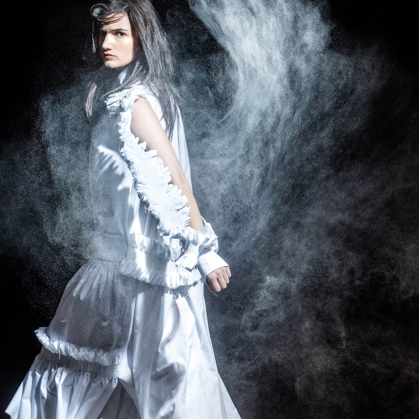 A model in a pale ruffled dress standing in swirling smoke.