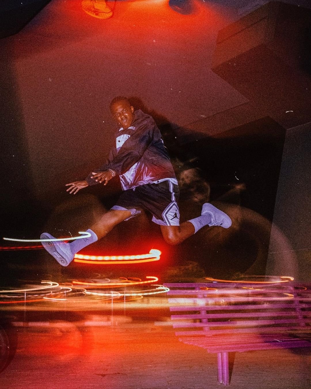 A dancer suspended above a city street with streaks of red and amber light.