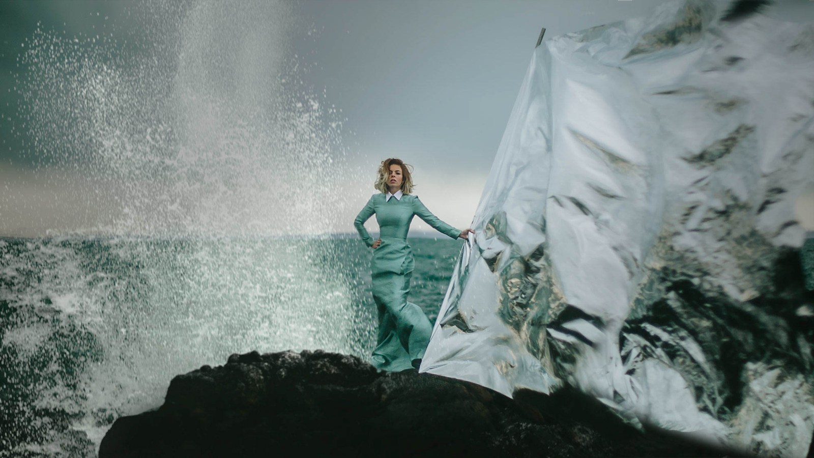 A figure in a flowing green dress standing in a pale, misty rock landscape.