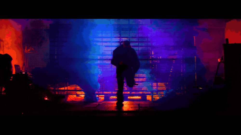 A dark figure moving through blue and magenta haze in front of a metal grid.