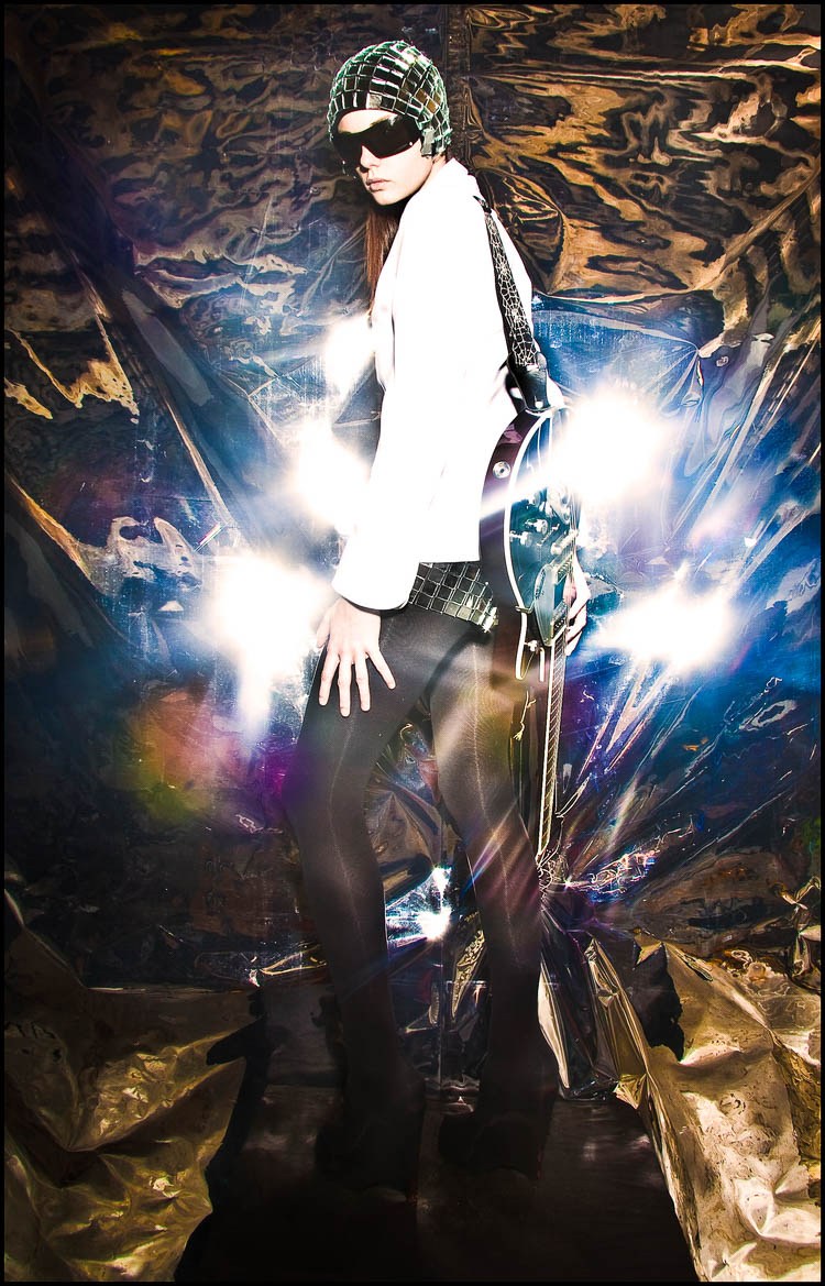 A model in sunglasses and metallic clothing surrounded by radiating flashes of light.