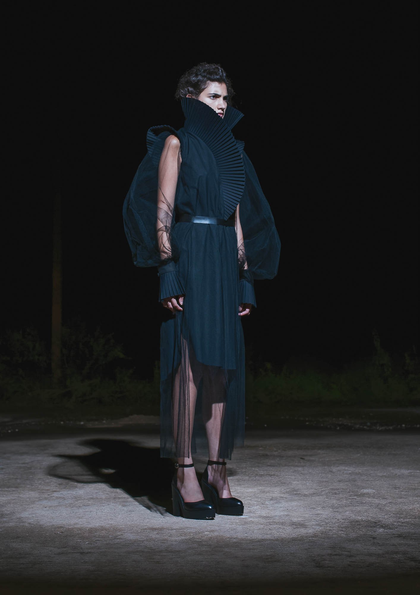 A runway model wearing a dark sleeveless outfit and a face covering.