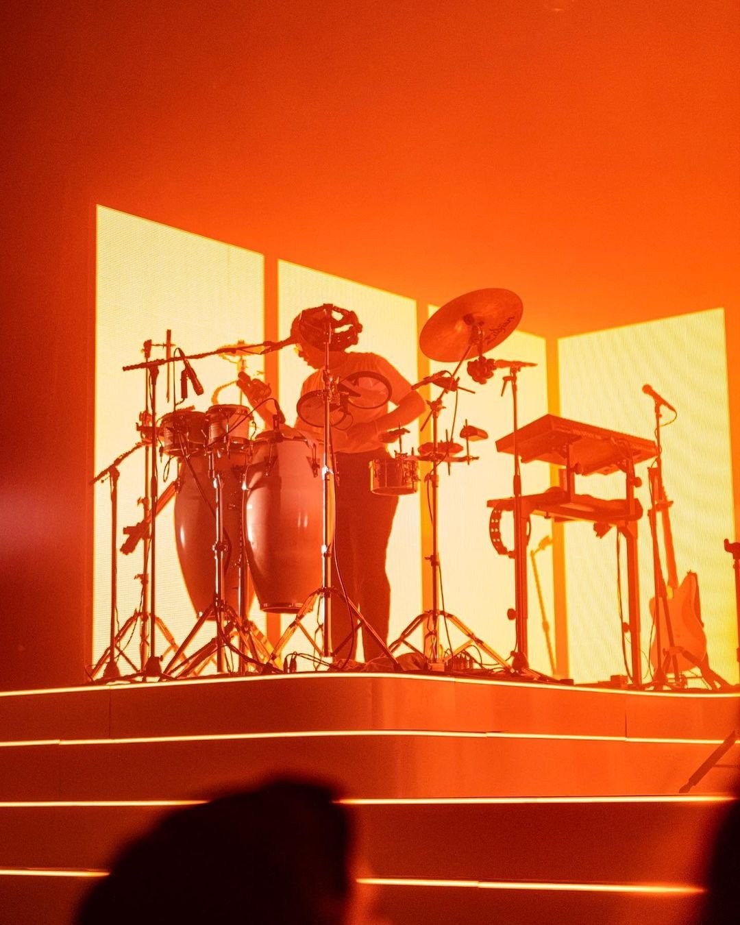 A drummer and drum kit silhouetted within a rectangular red-lit stage structure.