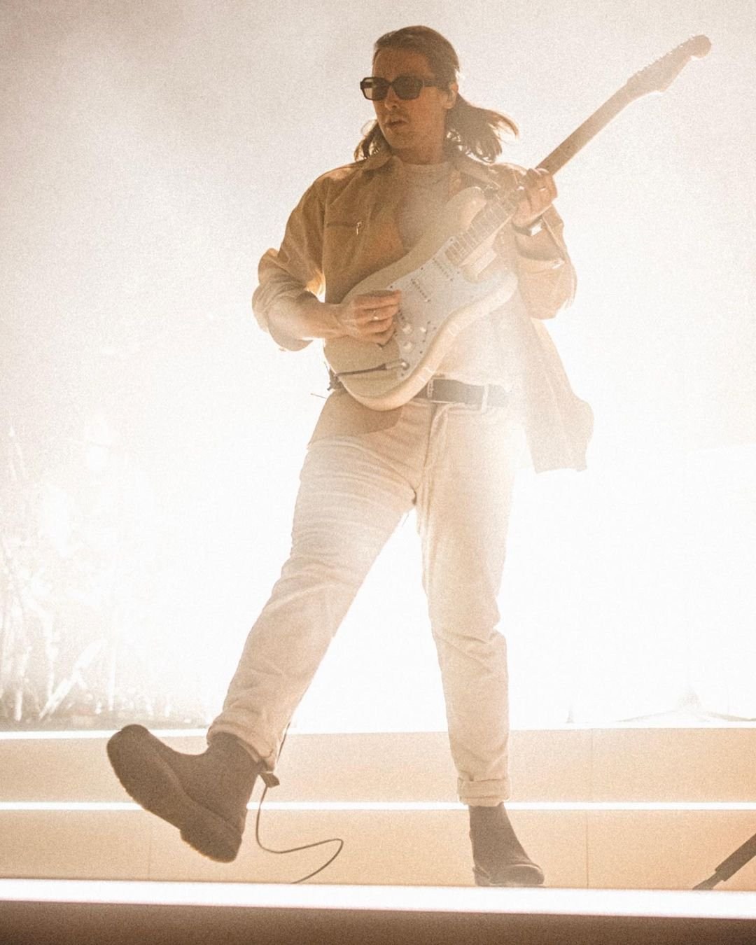 A performer in pale clothing walking across a brightly illuminated stage.