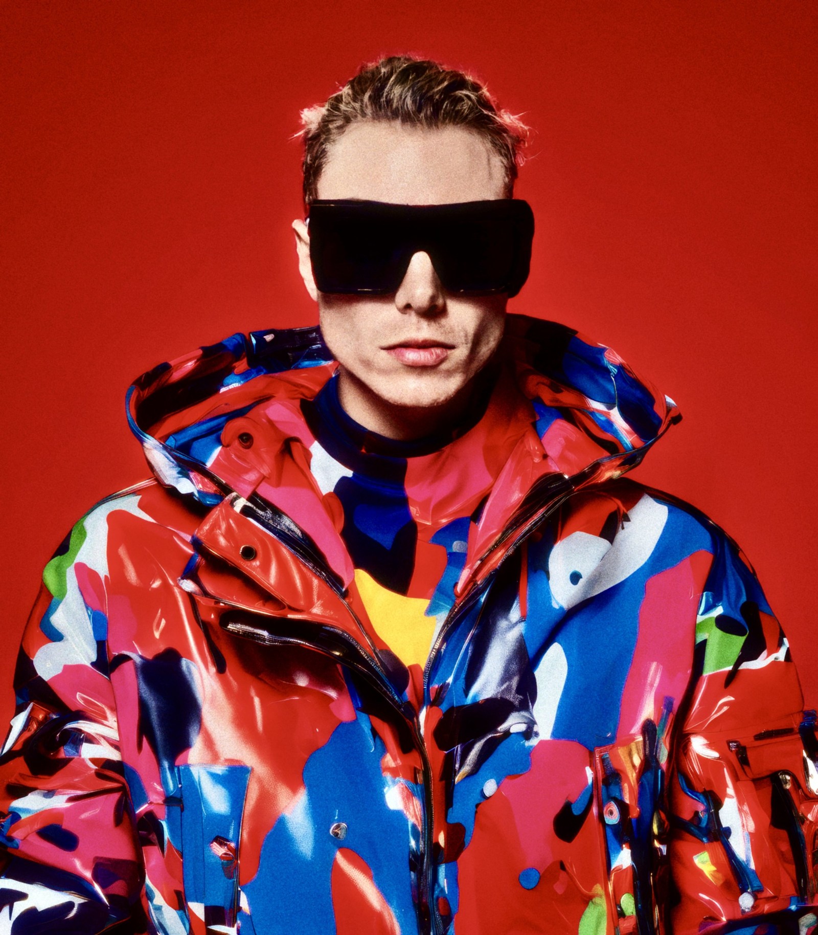 WORM in dark sunglasses and a vivid patterned jacket against red.