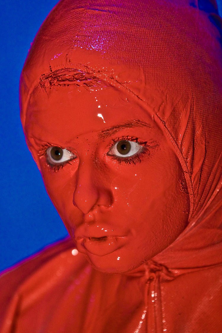 Close portrait of a face framed by a vivid red hood against blue.