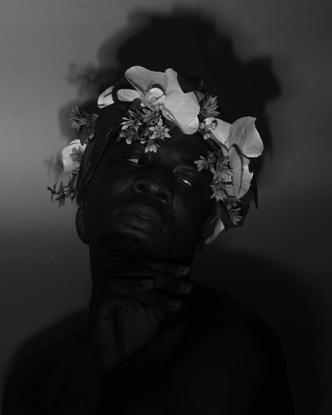 A dark black-and-white portrait of a model wearing a crown of pale flowers.