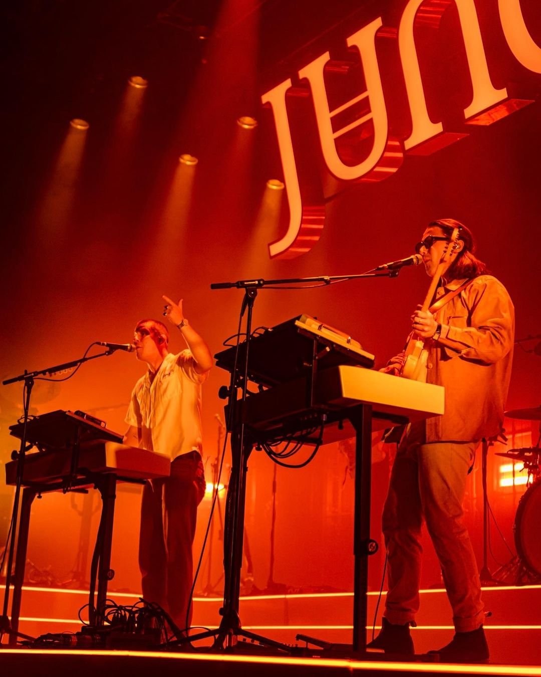 A low-angle view of a performer at a keyboard under orange-red stage lighting.