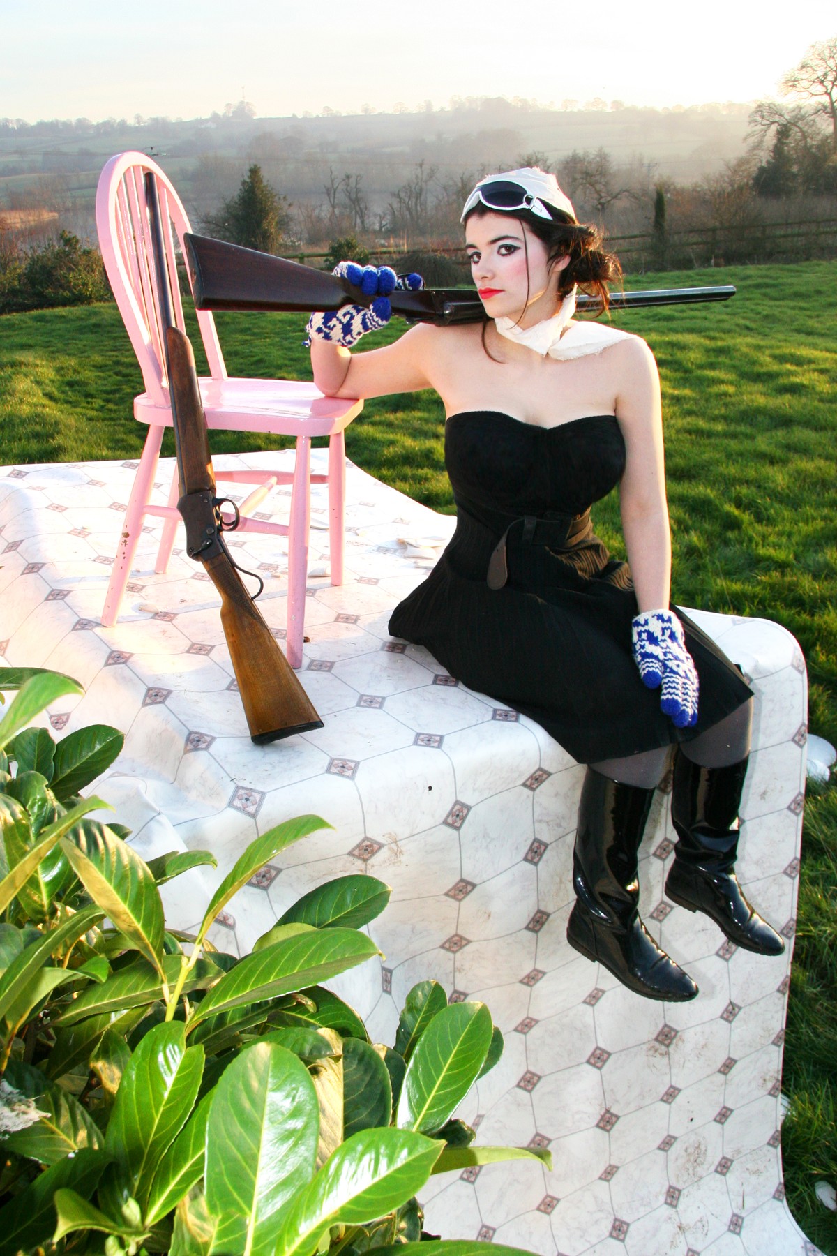 A woman in black beside a pink chair on a raised patterned platform in the countryside.