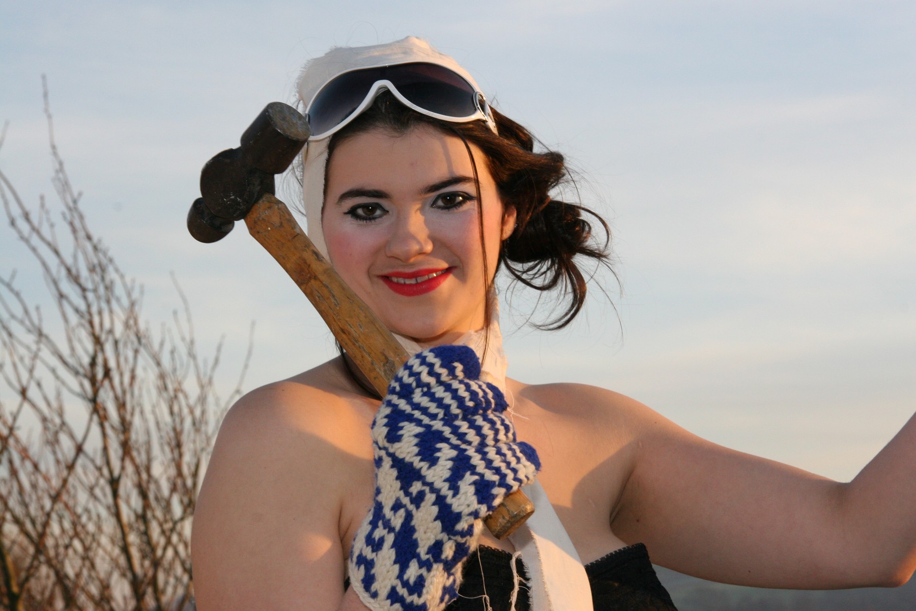 A smiling close portrait with white aviator goggles and blue patterned gloves.