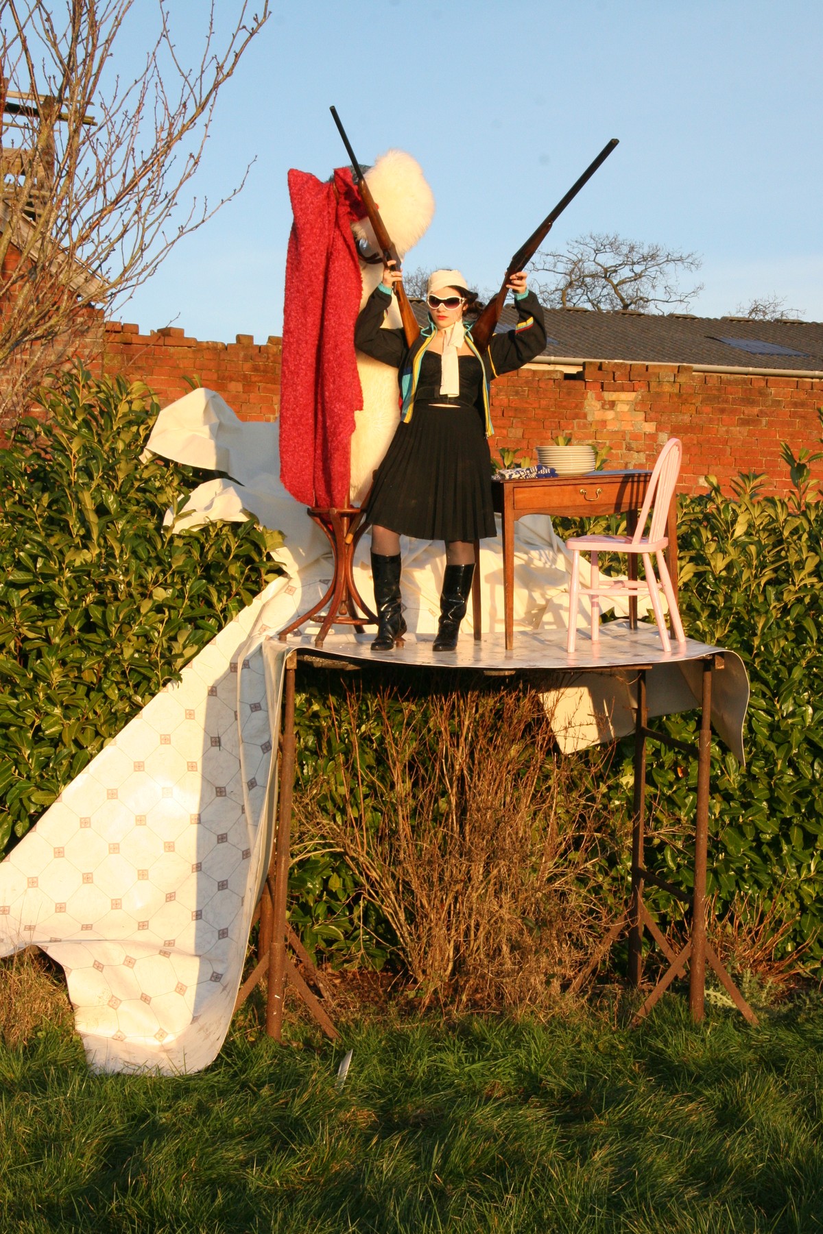 The garden stage in warm sunlight, with a figure, red drapery, a pink chair and hanging white fabric.