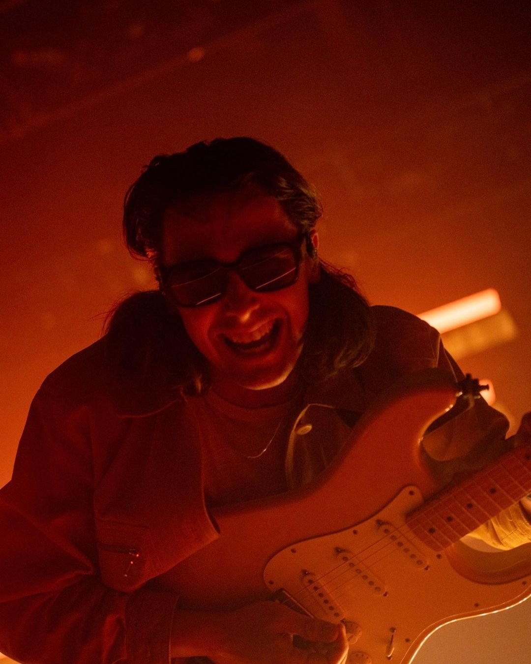 A close portrait of a performer leaning forward in deep red stage light.