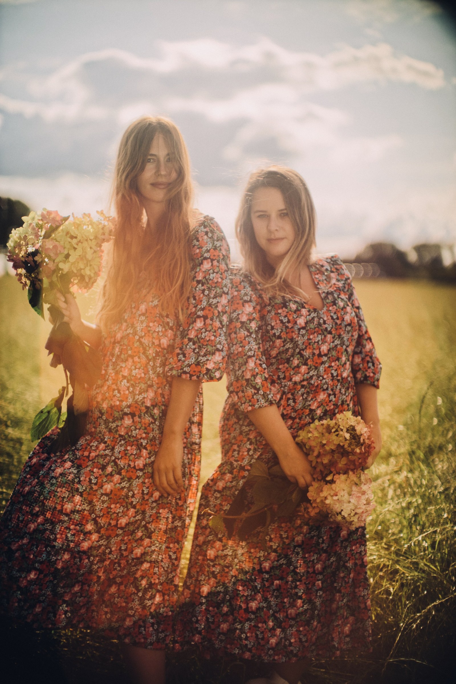 Two women standing in long grass in warm late-afternoon light.