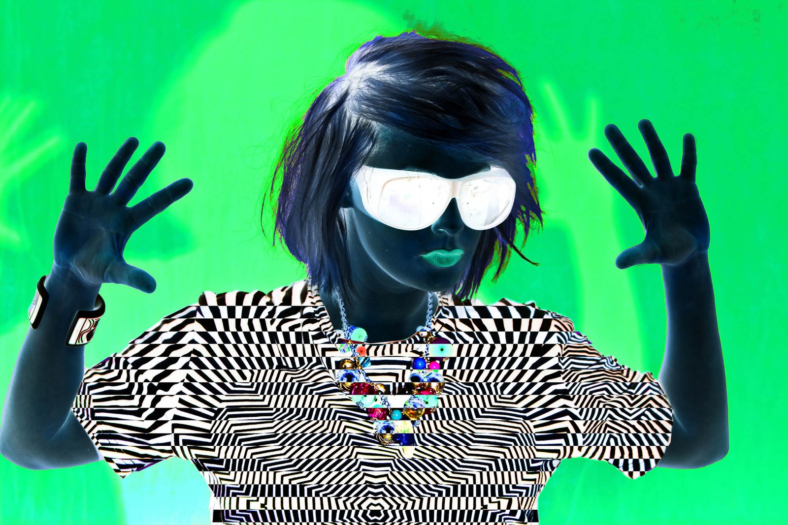 A model in reflective sunglasses and dark gloves holding up both hands against bright green.