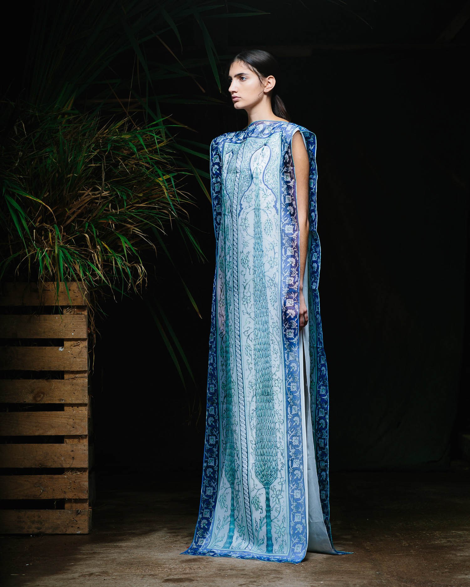A runway model in a floor-length blue dress with a shimmering vertical pattern.