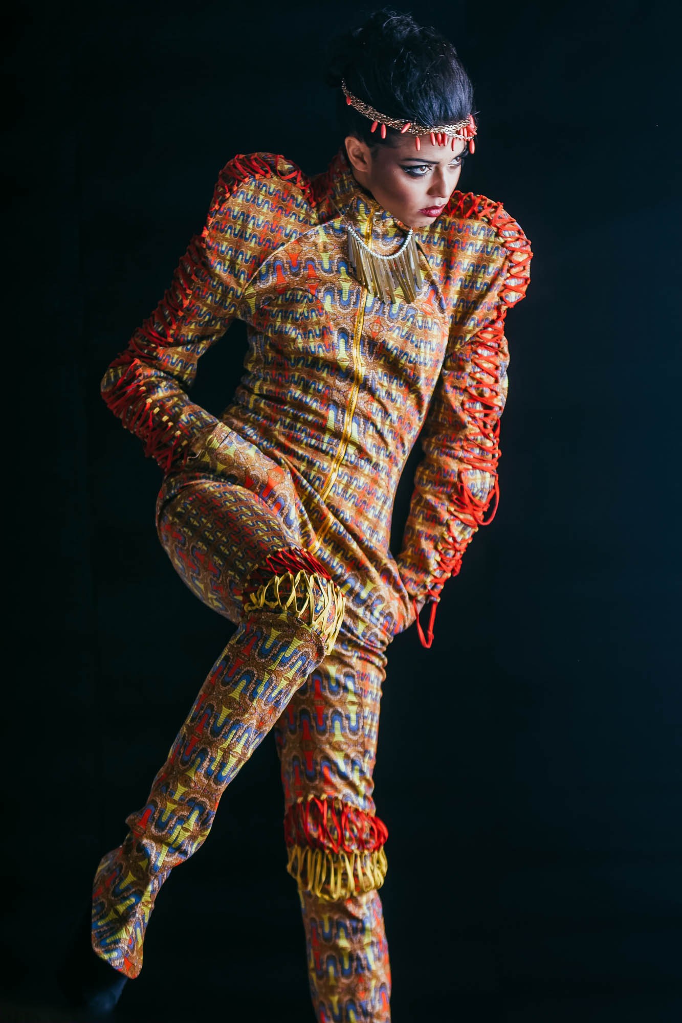 A model in a fitted multicoloured patterned suit against a dark studio background.