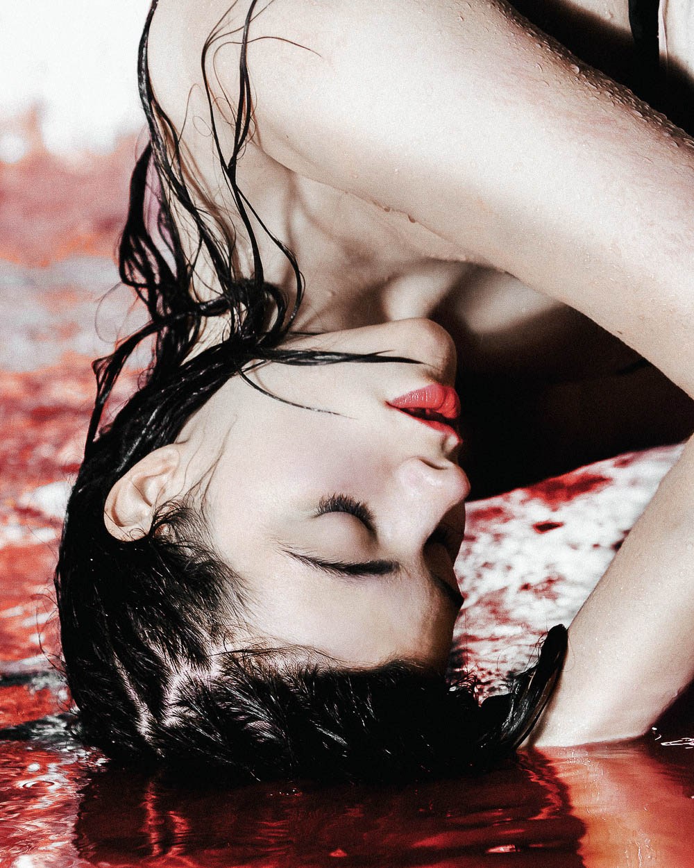 An upside-down close portrait of a model with wet dark hair and red lipstick.