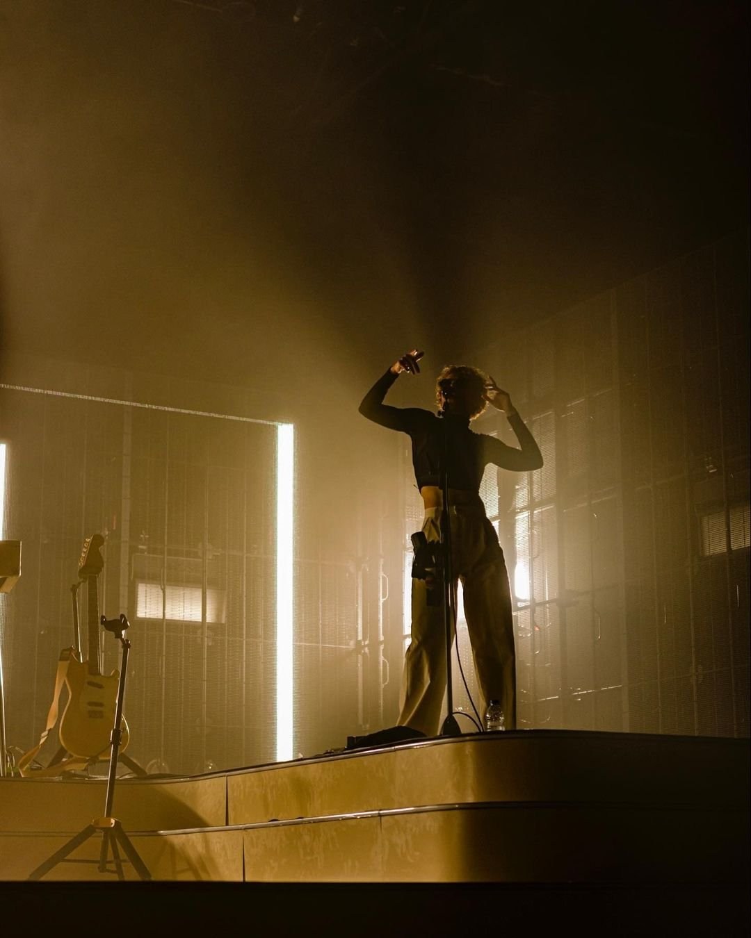 A distant performer framed by two tall white lights on a dark stage.
