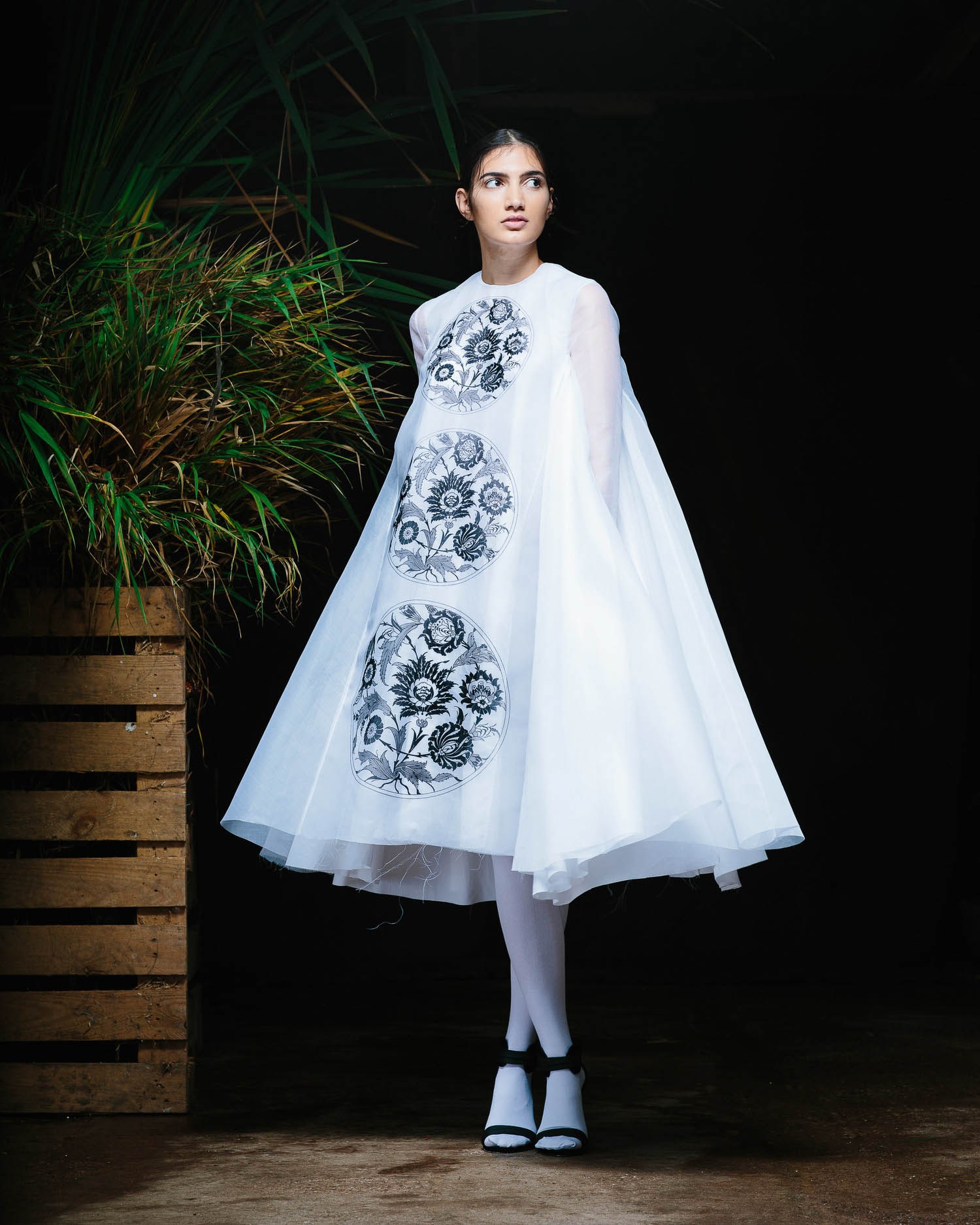 A runway model in a wide, pale printed dress and patterned tights.