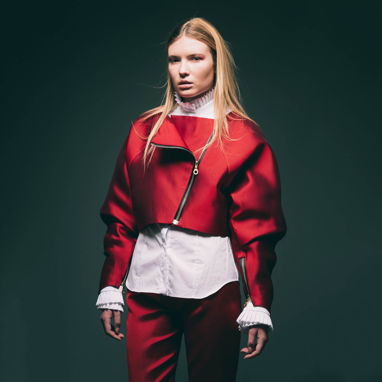 Front-facing studio portrait of a model in a layered red jacket and dark trousers.