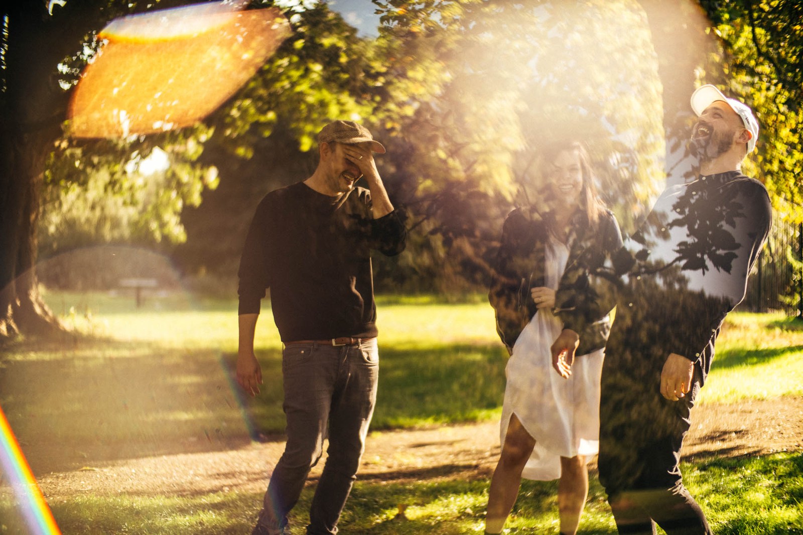 Three band members standing outdoors in bright, dappled sunlight.