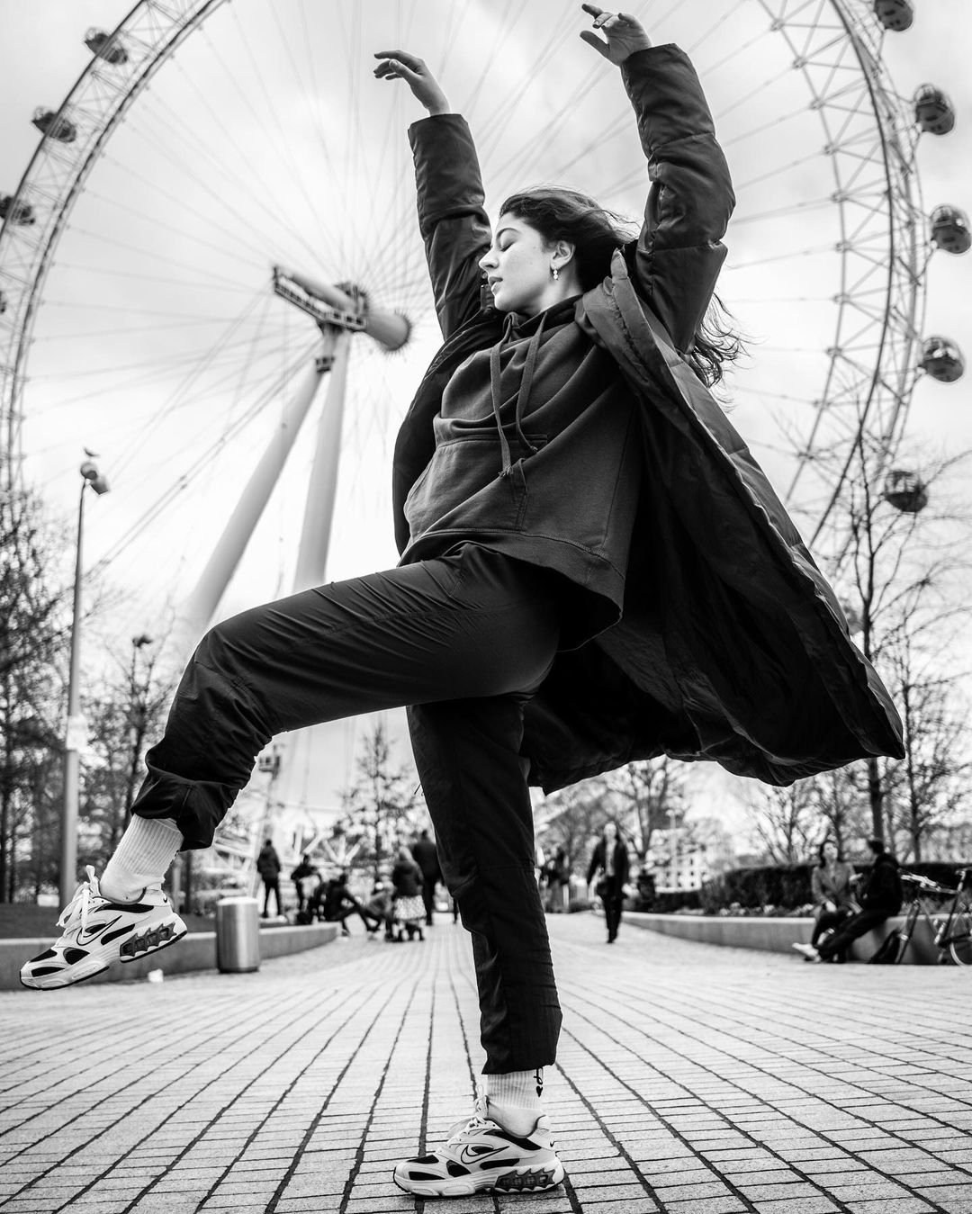 Black-and-white photograph of a dancer leaping beside a large observation wheel.
