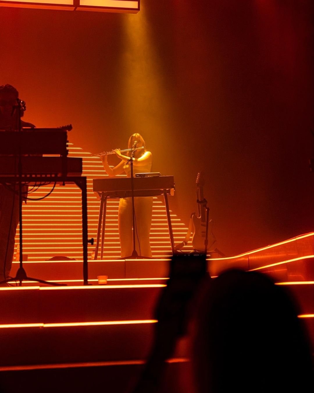 A side view of a keyboard performer silhouetted in orange stage light.