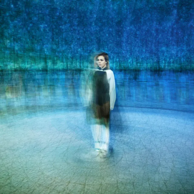 A solitary figure standing in a reflective blue-lit space.