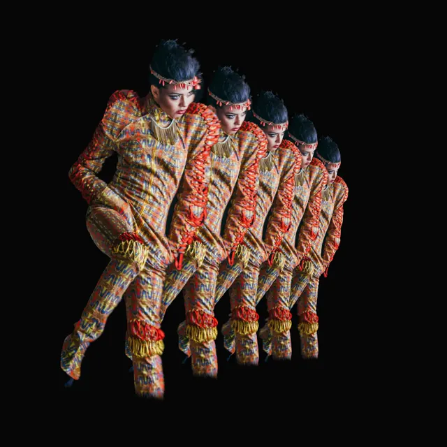 A model in a fitted multicoloured patterned suit against a dark studio background. Five figures repeat along a curved path in space as the viewpoint moves.