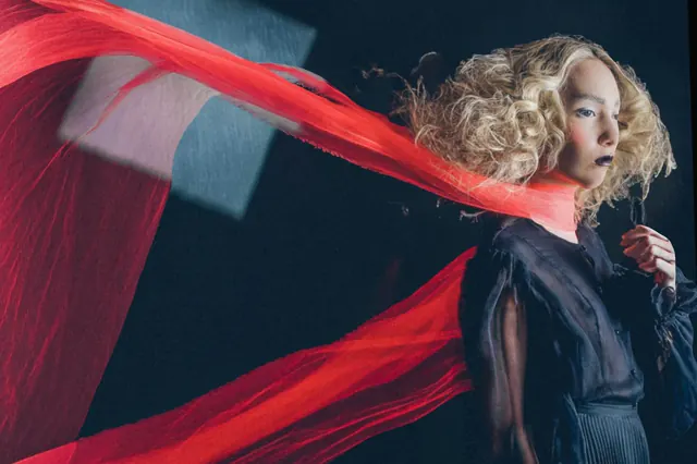 A model in dark clothing with a long red scarf sweeping across the image.